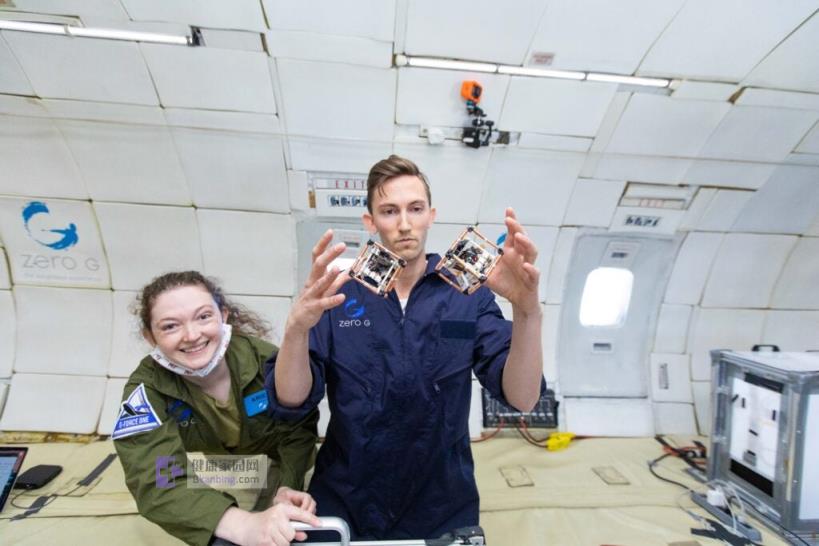 a woman and man in flight jumpsuits test two robotic cubes in low gravity enviro<em></em>nments on a plane