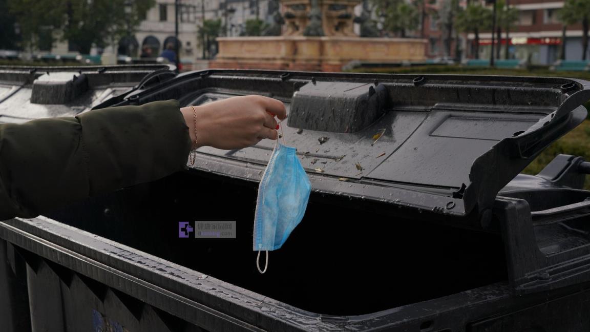 Person throwing COVID-19 disposable mask in trash can.